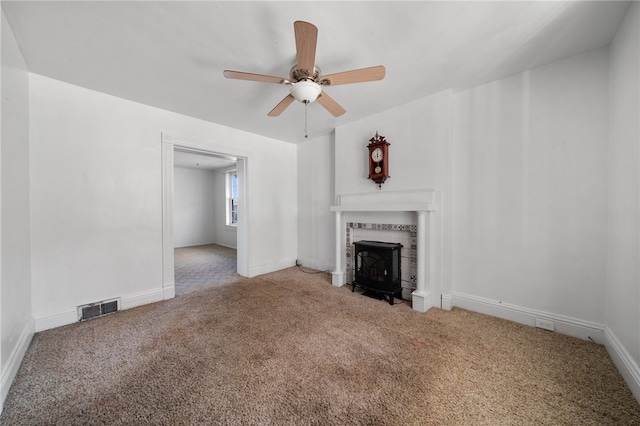 unfurnished living room featuring carpet, a wood stove, and ceiling fan