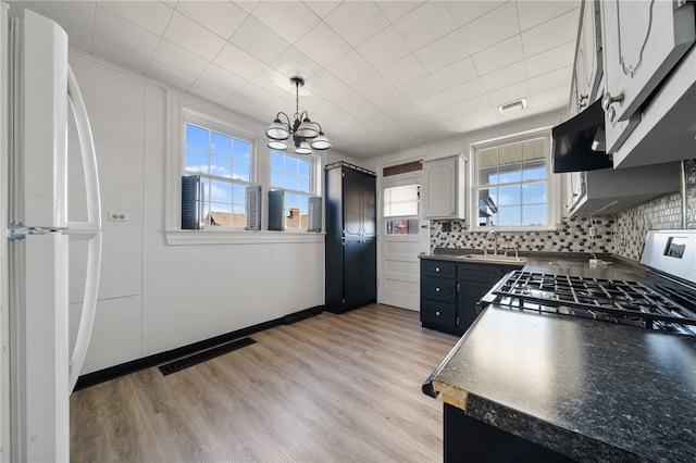 kitchen with backsplash, white refrigerator, exhaust hood, pendant lighting, and light hardwood / wood-style flooring