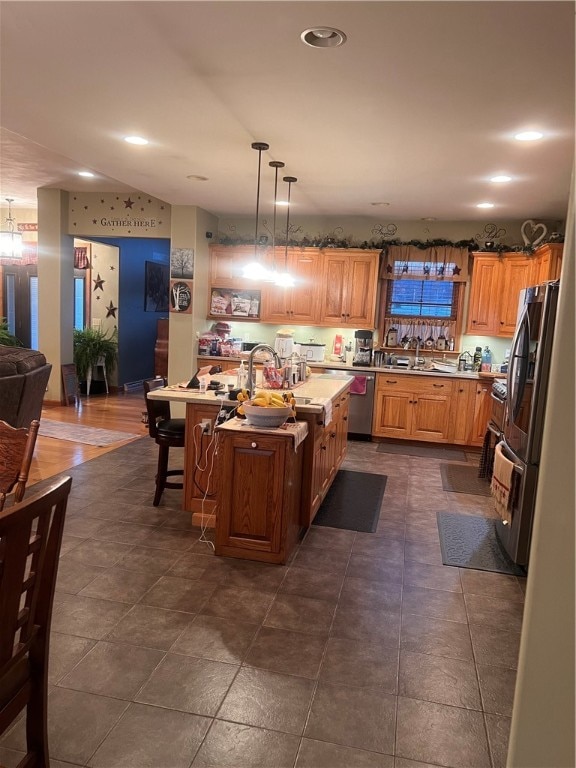 kitchen with sink, a kitchen bar, an island with sink, stainless steel appliances, and decorative light fixtures