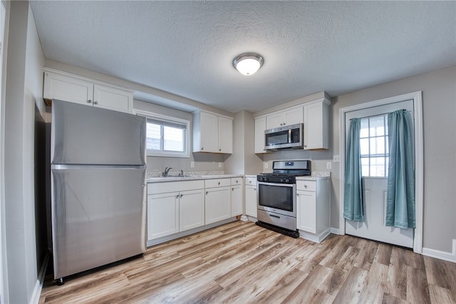 kitchen with sink, a textured ceiling, white cabinetry, light hardwood / wood-style floors, and stainless steel appliances