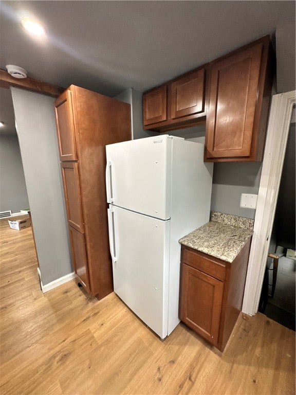 kitchen featuring light hardwood / wood-style flooring, light stone countertops, and white refrigerator