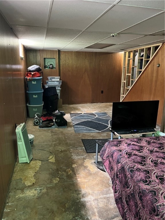 bedroom with a drop ceiling, wooden walls, and concrete flooring