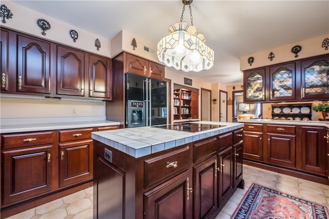 kitchen with a kitchen island, black appliances, pendant lighting, tile counters, and dark brown cabinetry