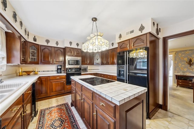 kitchen with a kitchen island, visible vents, hanging light fixtures, black appliances, and glass insert cabinets