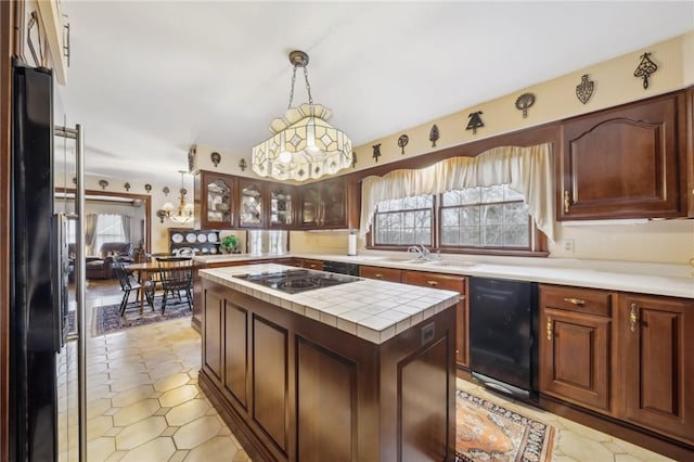 kitchen with glass insert cabinets, a center island, black appliances, pendant lighting, and a sink