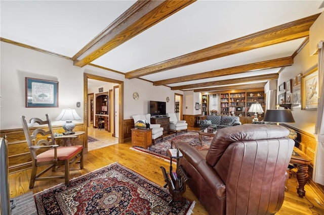 living room with built in shelves, beam ceiling, light wood-style floors, ornamental molding, and wainscoting