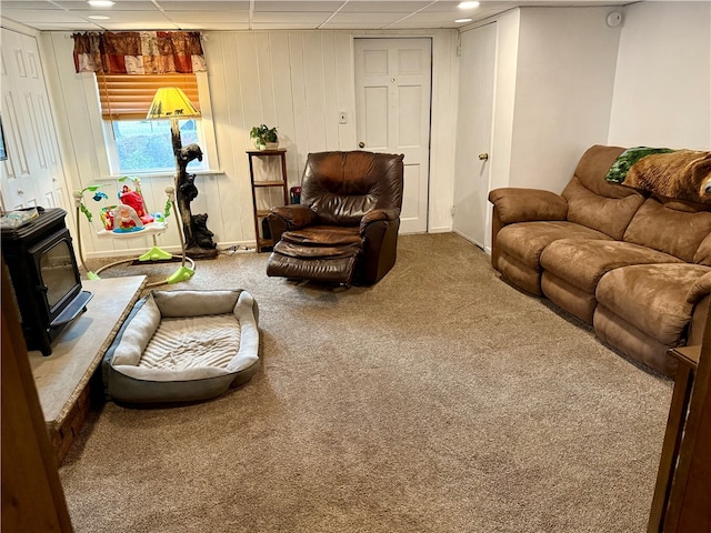 carpeted living room featuring a paneled ceiling and a wood stove