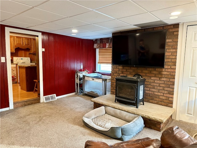 living room featuring a drop ceiling, a wood stove, wood walls, and carpet