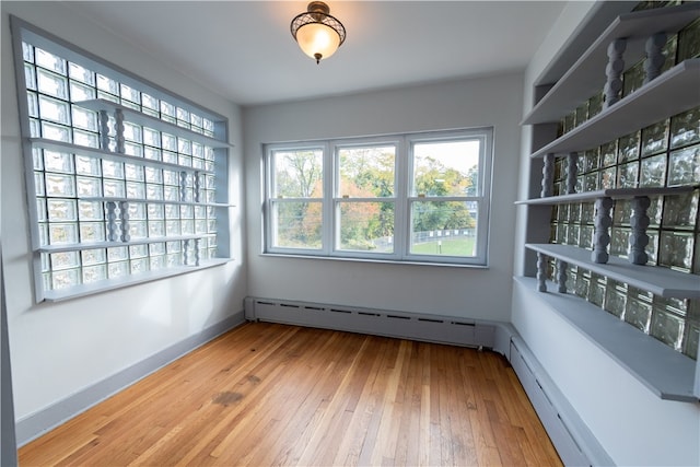 unfurnished room featuring baseboard heating, light wood-type flooring, and a healthy amount of sunlight