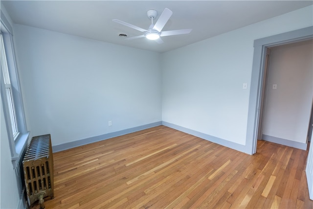 empty room featuring radiator, ceiling fan, and light hardwood / wood-style flooring