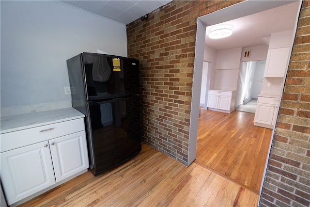 kitchen with black fridge, light hardwood / wood-style flooring, brick wall, white cabinetry, and light stone counters