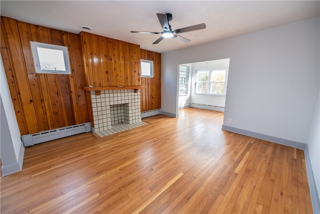 unfurnished living room featuring a tiled fireplace, wooden walls, baseboard heating, and light hardwood / wood-style floors