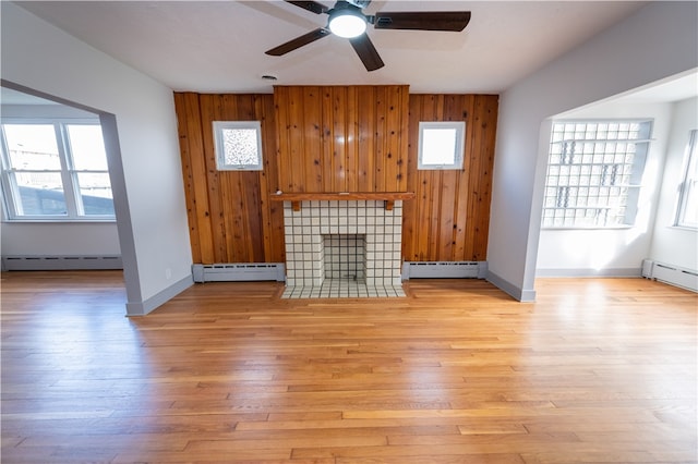 unfurnished living room with baseboard heating, light hardwood / wood-style flooring, a fireplace, and wood walls