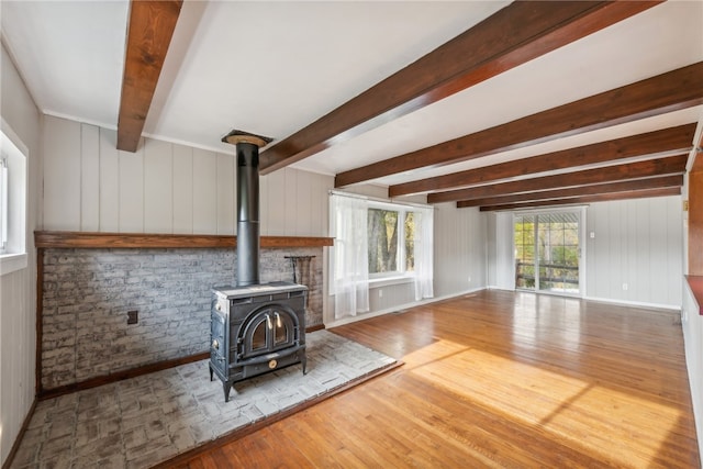 unfurnished living room with beamed ceiling, hardwood / wood-style floors, a wood stove, and wooden walls