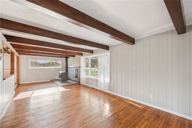 unfurnished living room featuring a wood stove, wood walls, beam ceiling, and light wood-type flooring