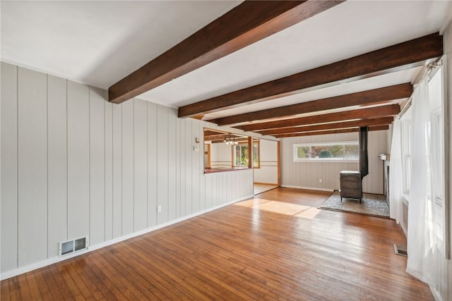 unfurnished living room with beam ceiling, wood walls, and light hardwood / wood-style flooring