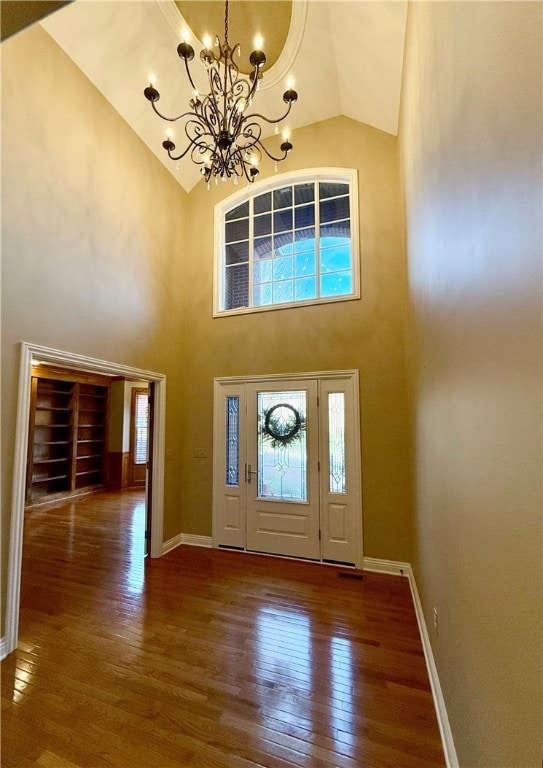 entryway with high vaulted ceiling, an inviting chandelier, and dark hardwood / wood-style floors