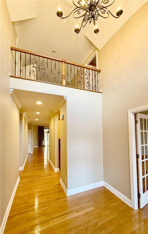 corridor with crown molding, a notable chandelier, wood-type flooring, and a towering ceiling