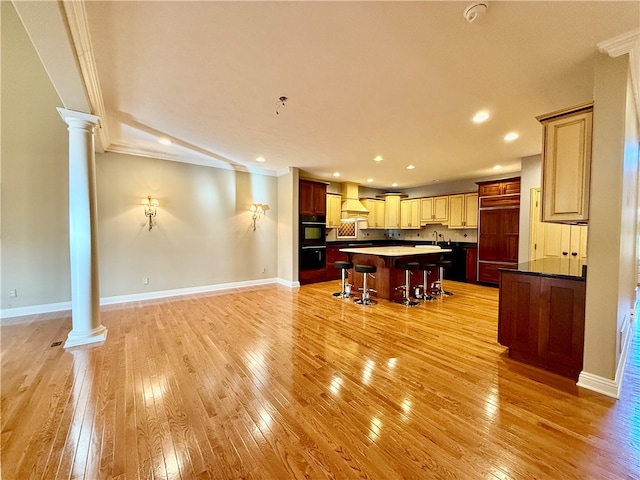 kitchen featuring a breakfast bar area, a kitchen island, light wood-type flooring, ornate columns, and crown molding