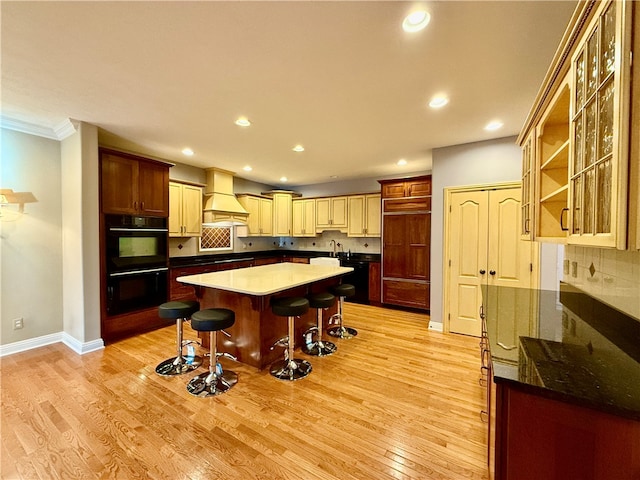 kitchen with black appliances, sink, a kitchen bar, light hardwood / wood-style flooring, and premium range hood