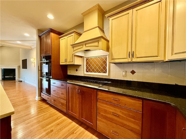 kitchen with double oven, electric stovetop, backsplash, custom exhaust hood, and light hardwood / wood-style floors