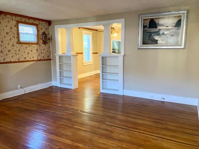 spare room with dark wood-type flooring, crown molding, a textured ceiling, and decorative columns