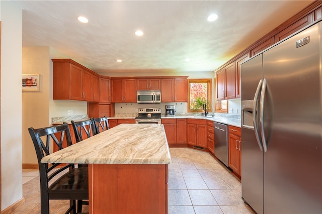 kitchen with appliances with stainless steel finishes, light stone counters, a breakfast bar, a kitchen island, and light tile patterned flooring