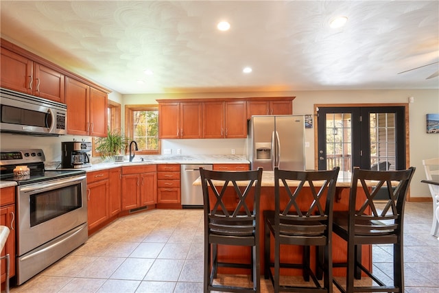 kitchen featuring ceiling fan, sink, stainless steel appliances, a kitchen bar, and a kitchen island