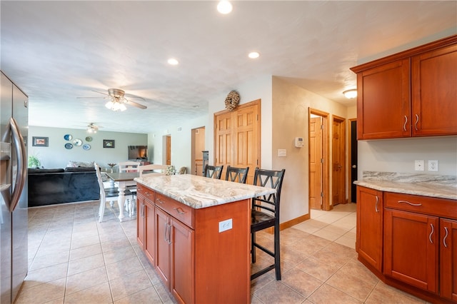 kitchen featuring a center island, stainless steel fridge with ice dispenser, light stone counters, a kitchen bar, and light tile patterned flooring