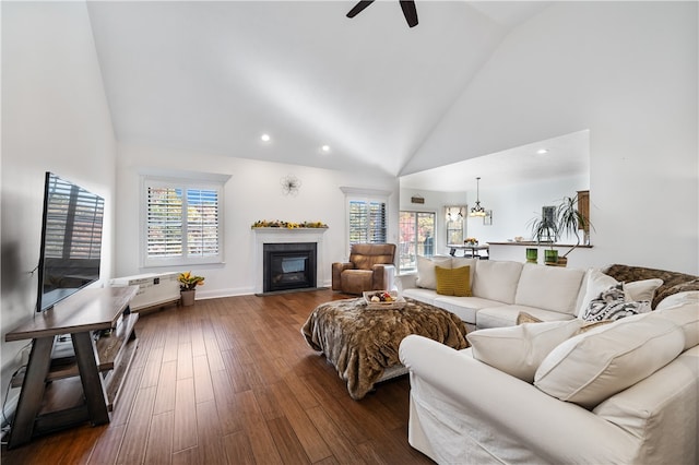 living room with a wealth of natural light, ceiling fan with notable chandelier, high vaulted ceiling, and dark hardwood / wood-style flooring