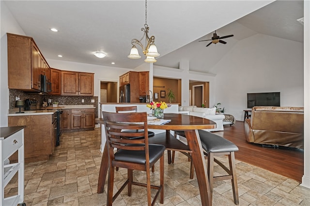 dining area featuring high vaulted ceiling, sink, light wood-type flooring, and ceiling fan with notable chandelier