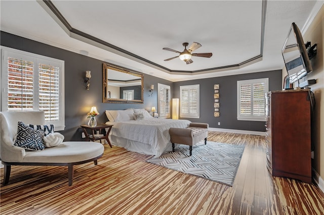 bedroom with ceiling fan, a raised ceiling, wood-type flooring, and multiple windows