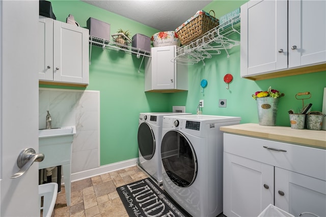 laundry room featuring washer and dryer, a textured ceiling, and cabinets