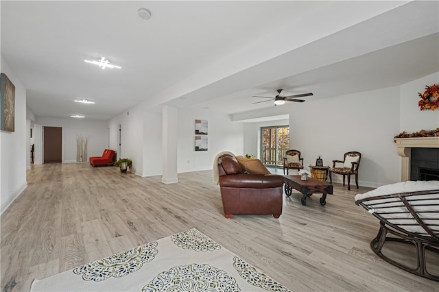 living room with a tiled fireplace, light wood-type flooring, and ceiling fan