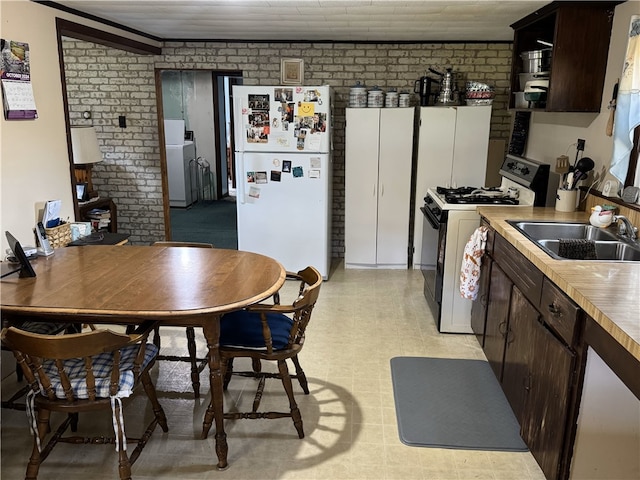 kitchen with washer / clothes dryer, dark brown cabinets, brick wall, sink, and white appliances