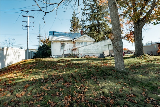 rear view of house with a chimney, a lawn, fence, and metal roof