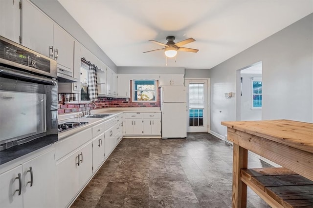 kitchen with stainless steel gas stovetop, white cabinets, tasteful backsplash, black oven, and white fridge