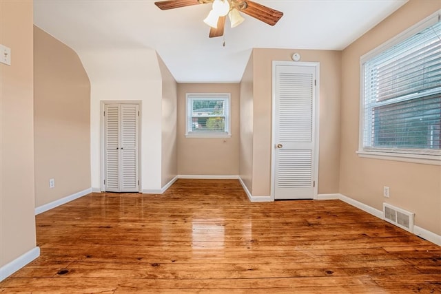 unfurnished bedroom with wood-type flooring, ceiling fan, and multiple closets