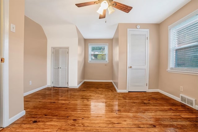 unfurnished bedroom featuring hardwood / wood-style floors, multiple windows, and multiple closets