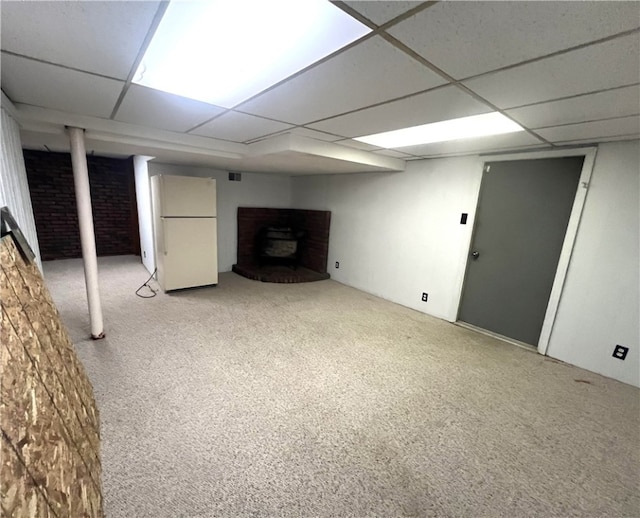 basement featuring a drop ceiling, a wood stove, light carpet, and white refrigerator