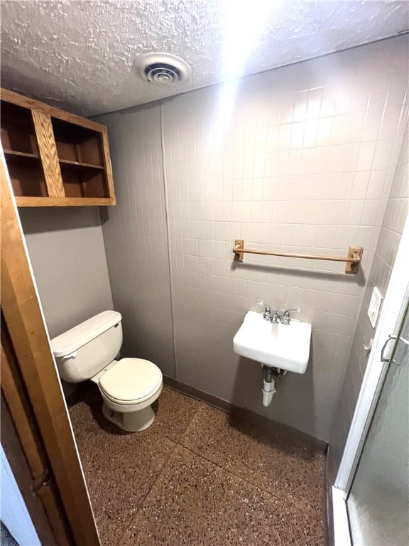 bathroom with toilet, a textured ceiling, sink, and a shower with door