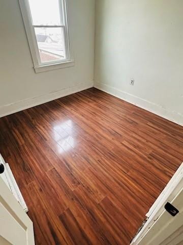 spare room with baseboards and wood finished floors