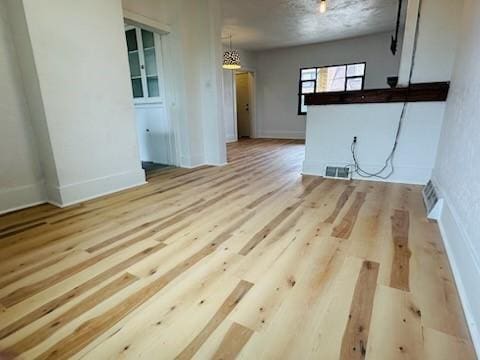 unfurnished living room with wood finished floors, visible vents, and baseboards