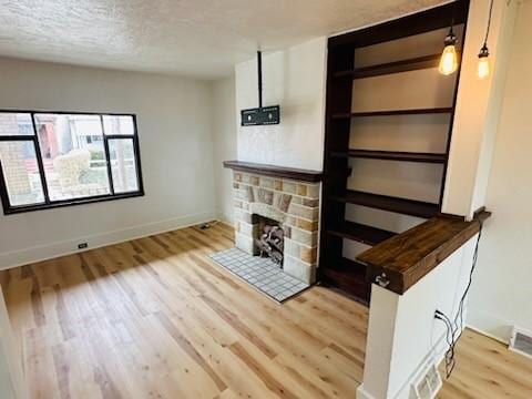 unfurnished living room featuring a textured ceiling, a fireplace, baseboards, and wood finished floors