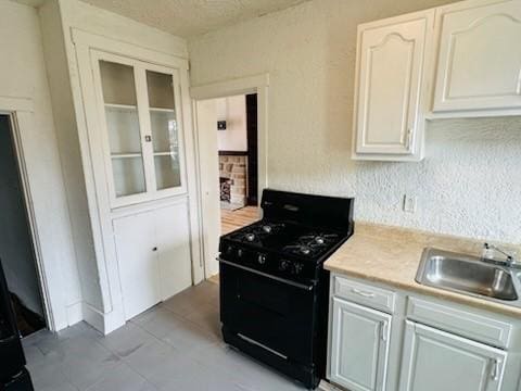 kitchen with a textured wall, gas stove, light countertops, and a sink