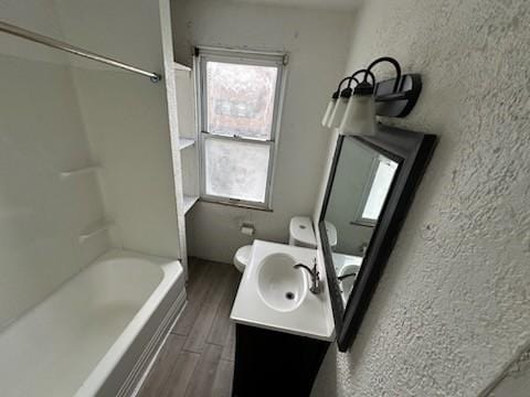 bathroom with shower / washtub combination, a textured wall, toilet, vanity, and wood finished floors