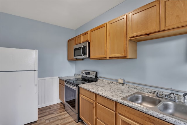 kitchen with stainless steel appliances, light stone countertops, sink, and light wood-type flooring