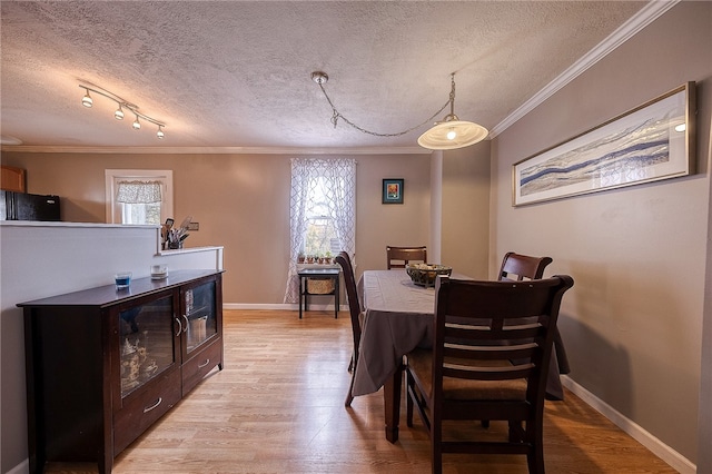 dining space featuring rail lighting, a textured ceiling, ornamental molding, and light wood-type flooring