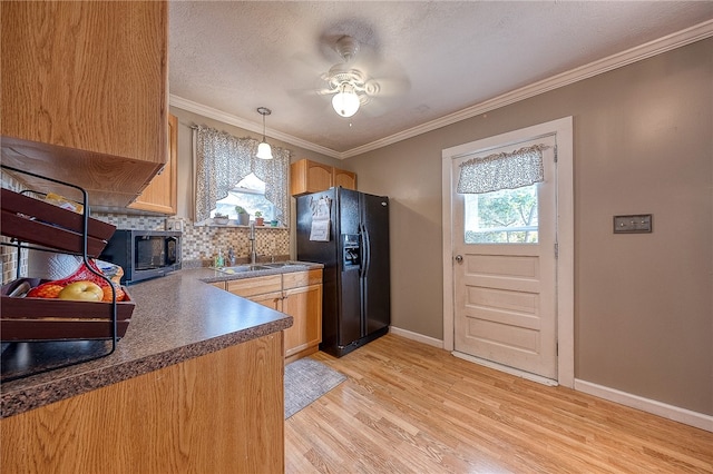 kitchen featuring sink, black fridge, hanging light fixtures, crown molding, and light hardwood / wood-style flooring