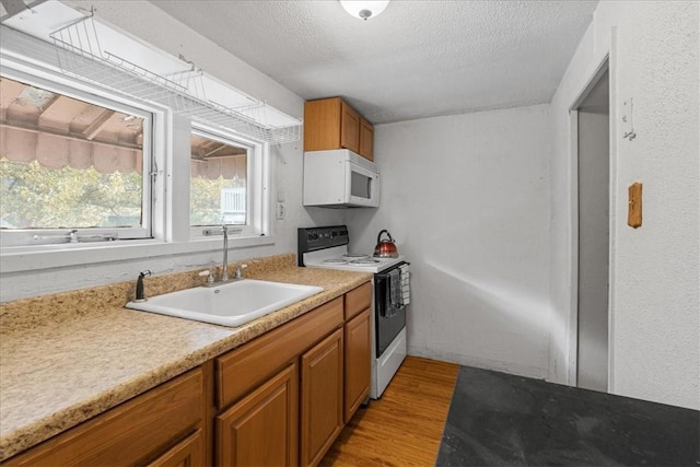 kitchen featuring a textured ceiling, sink, white appliances, and light hardwood / wood-style flooring